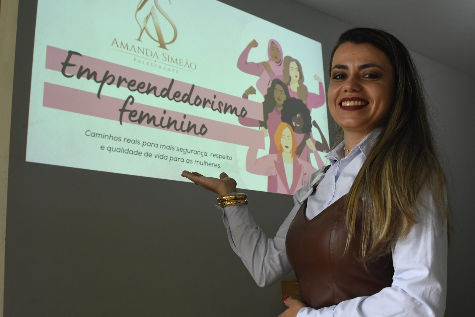 Amanda Simeão palestrando ao lado do slide de abertura da palestra Empreendedorismo Feminino